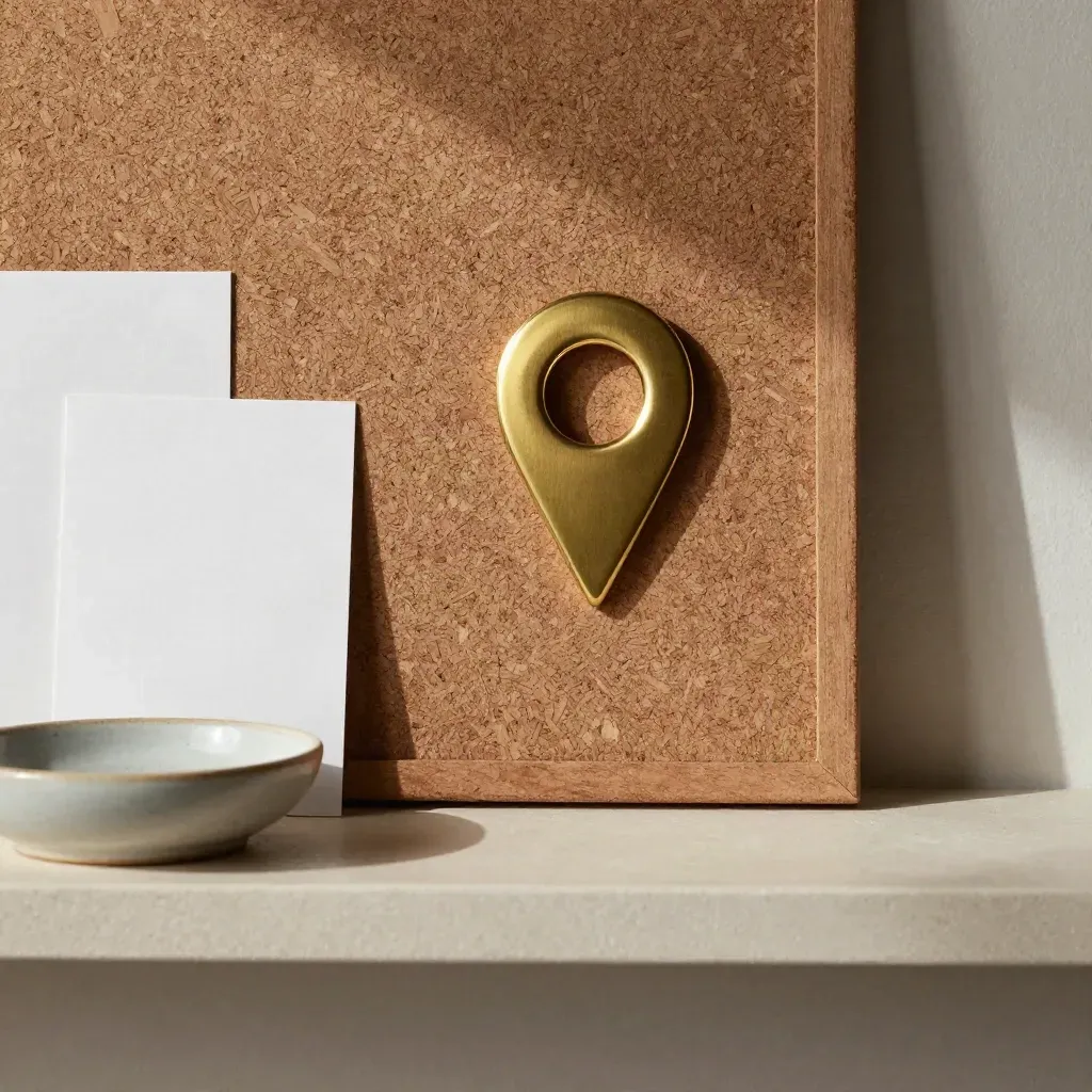Brass location pin, cork board, key dish and blank cards on a pale shelf.